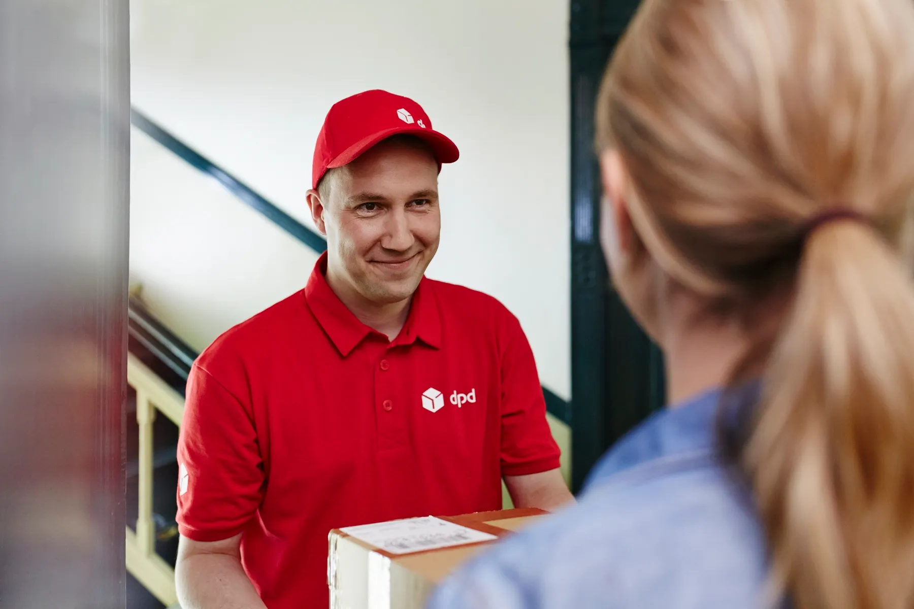 dpd-Zusteller übergibt einer Kundin lächelnd ein Paket